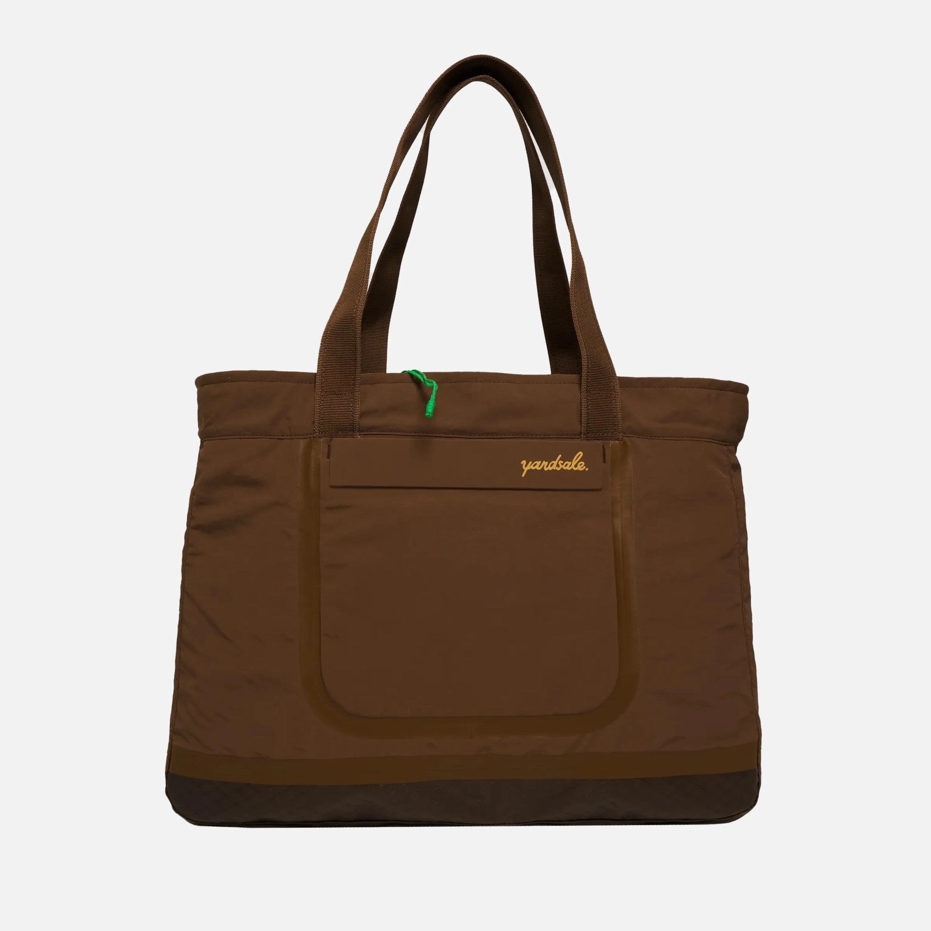 Brown tote bag with two handles, a front pocket featuring a flap with the word "yardsale" embroidered in yellow, and a small green loop detail near the top. The bottom edge of the bag is slightly darker brown.