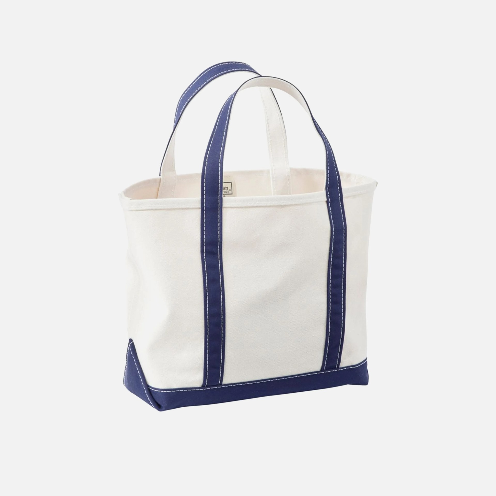 Canvas tote bag in off-white with navy blue handles, bottom, and corner reinforcements. The bag has visible white stitching along the navy blue sections.