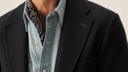 Close-up of a person wearing a navy blue blazer over a light blue denim shirt with snap buttons, and a black and white paisley-patterned scarf tucked inside the shirt collar.