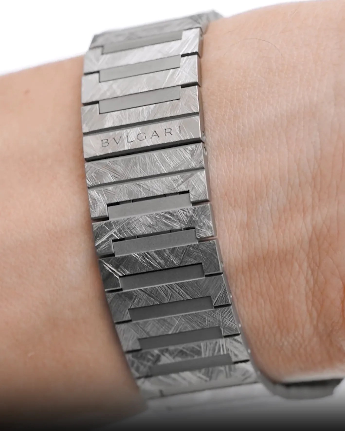 Metal watch bracelet with a brushed and textured finish, featuring the engraved brand name "BVLGARI" on one of the links. The bracelet is worn on a wrist.