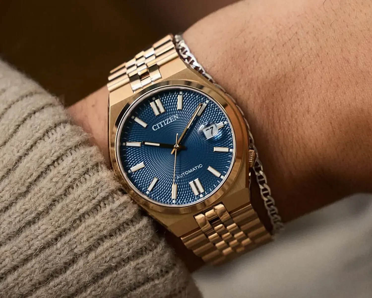 Gold-tone Citizen wristwatch with a textured blue dial, featuring gold hour markers and hands, a date window at the 3 o'clock position with a magnifier, and a matching gold metal bracelet.