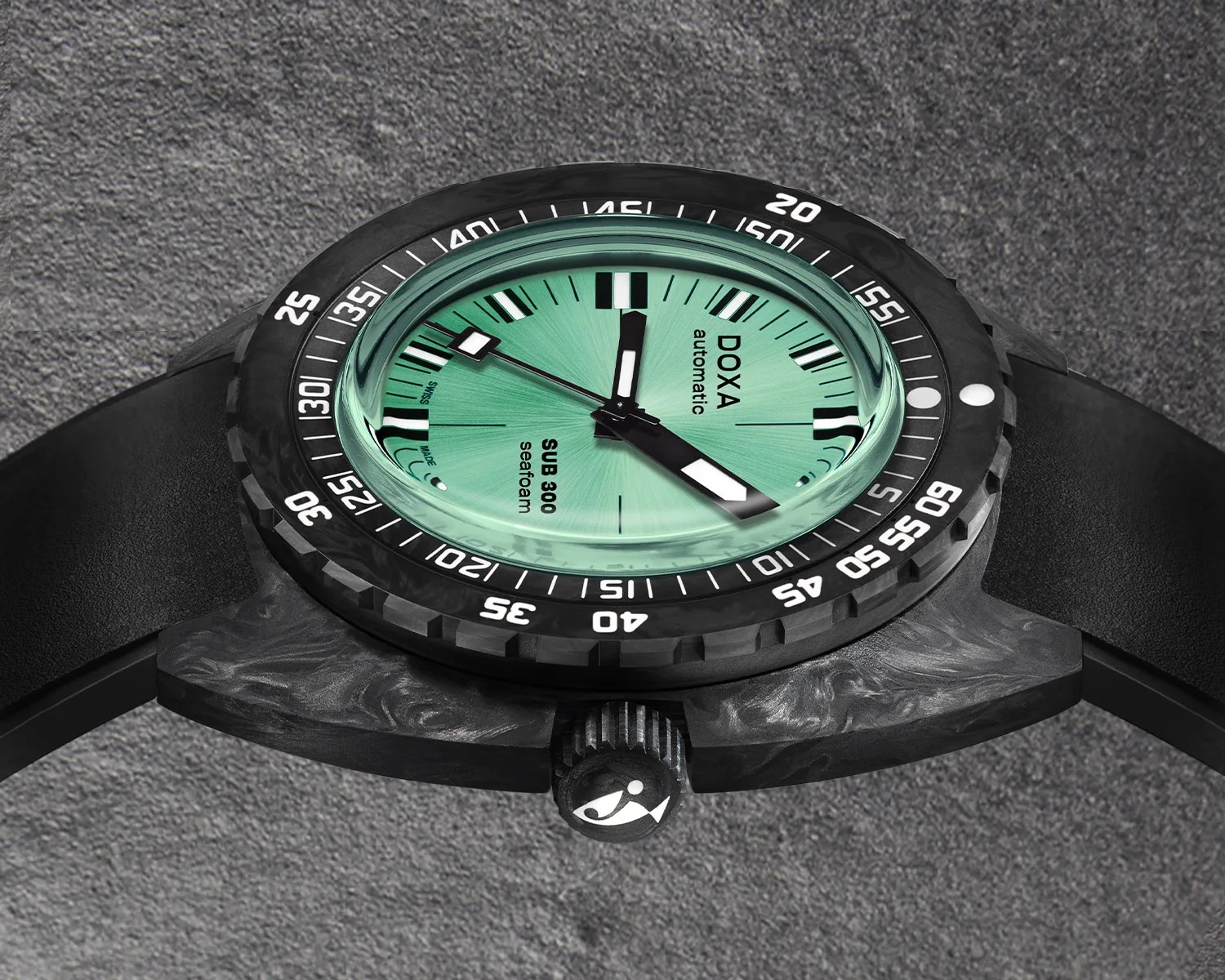 Black Doxa SUB 300 Seafoam automatic watch with a textured black bezel featuring white numerals and markers, a mint green dial with black and white hour markers and hands, and a black strap, displayed on a gray textured surface.