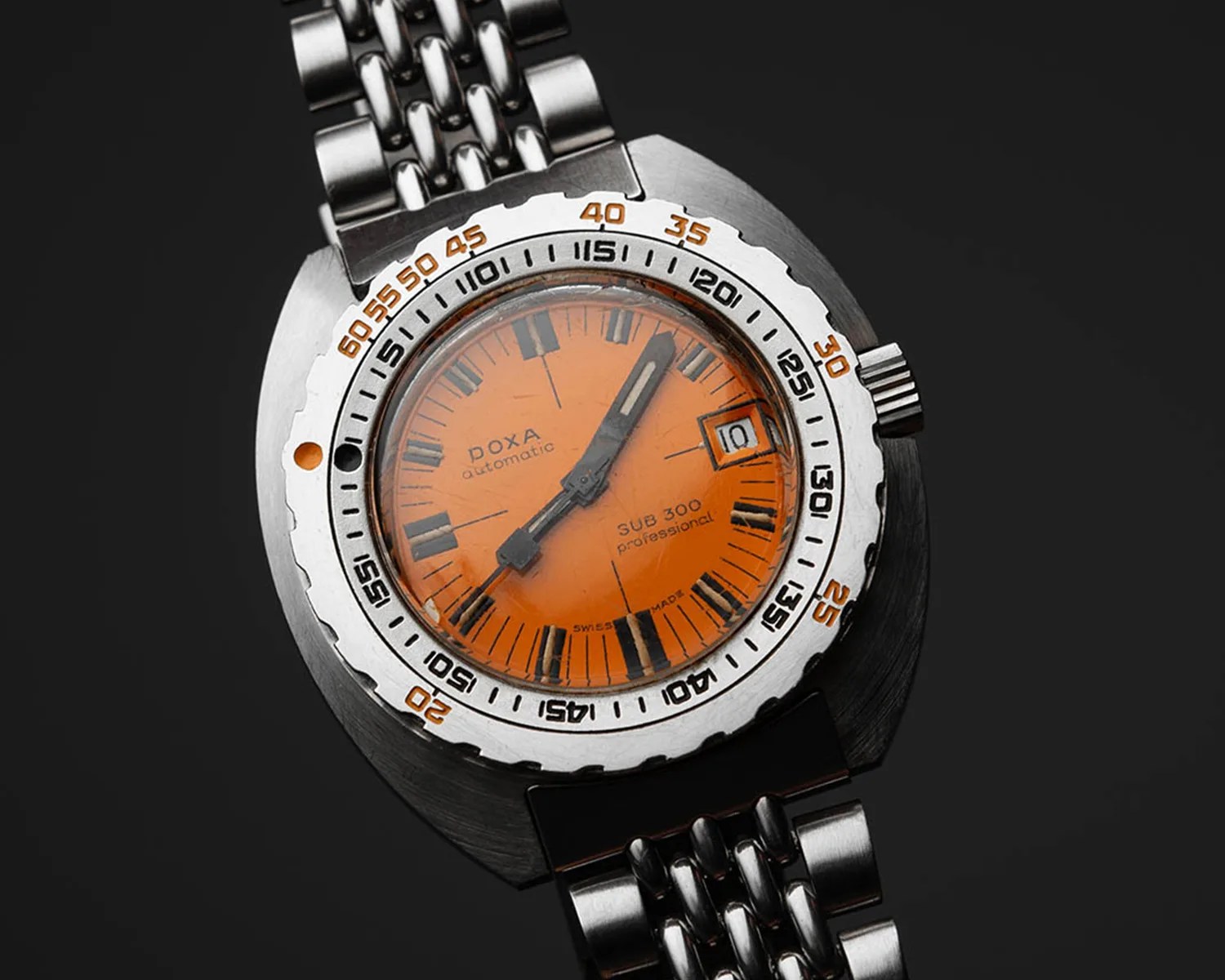 Stainless steel wristwatch with a bright orange dial, black Roman numeral hour markers, and a date window at the 3 o'clock position. The watch has a rotating bezel with black and orange minute markers and a metal link bracelet. The dial is marked with "DOXA automatic," "SUB 300 professional," and "SWISS MADE." The hour and minute hands are black with luminous inserts.