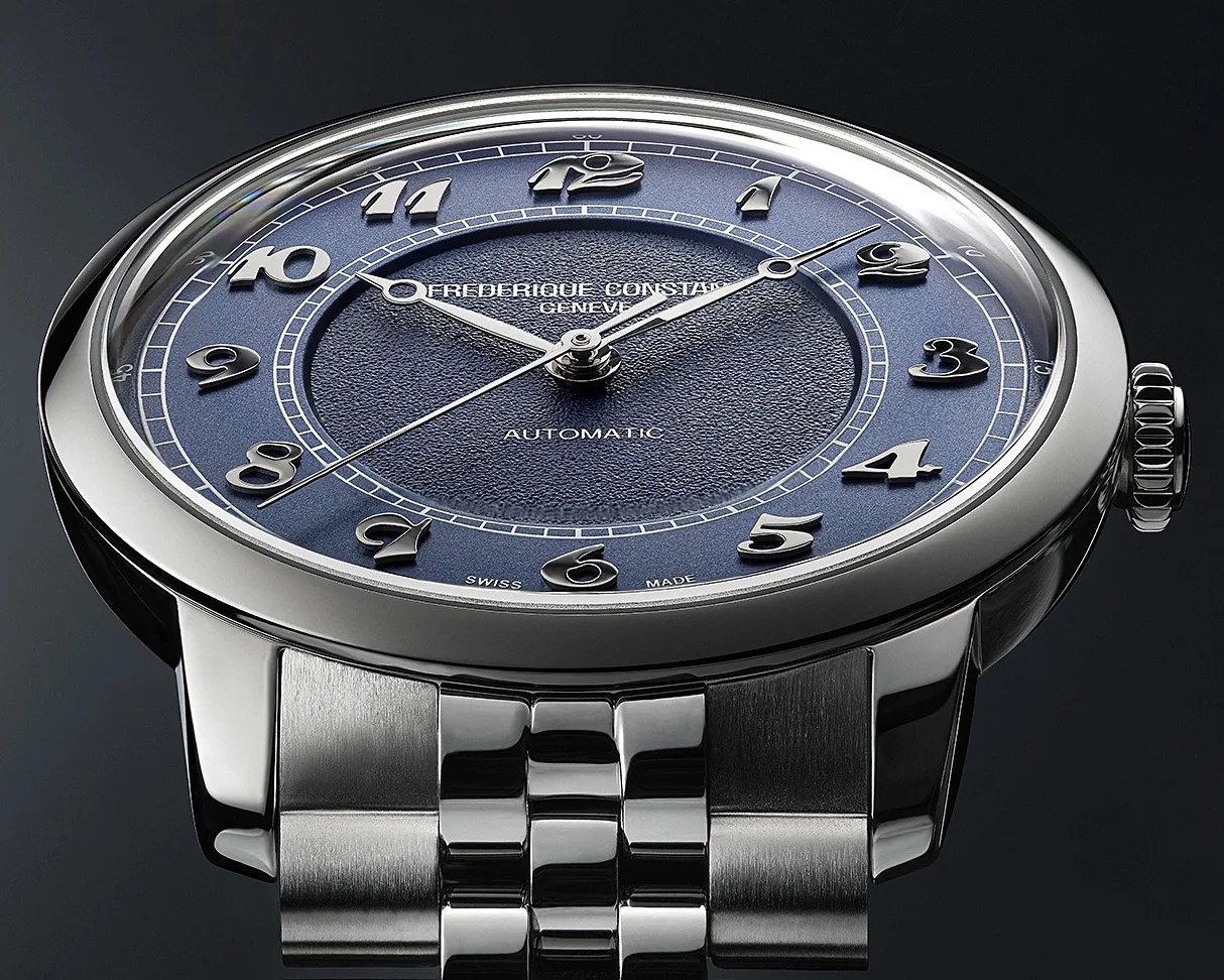 Silver wristwatch with a textured blue dial featuring raised silver Arabic numerals and three silver hands. The dial displays the text "FREDERIQUE CONSTANT GENEVE," "AUTOMATIC," and "SWISS MADE." The watch has a polished stainless steel case and a matching metal bracelet.