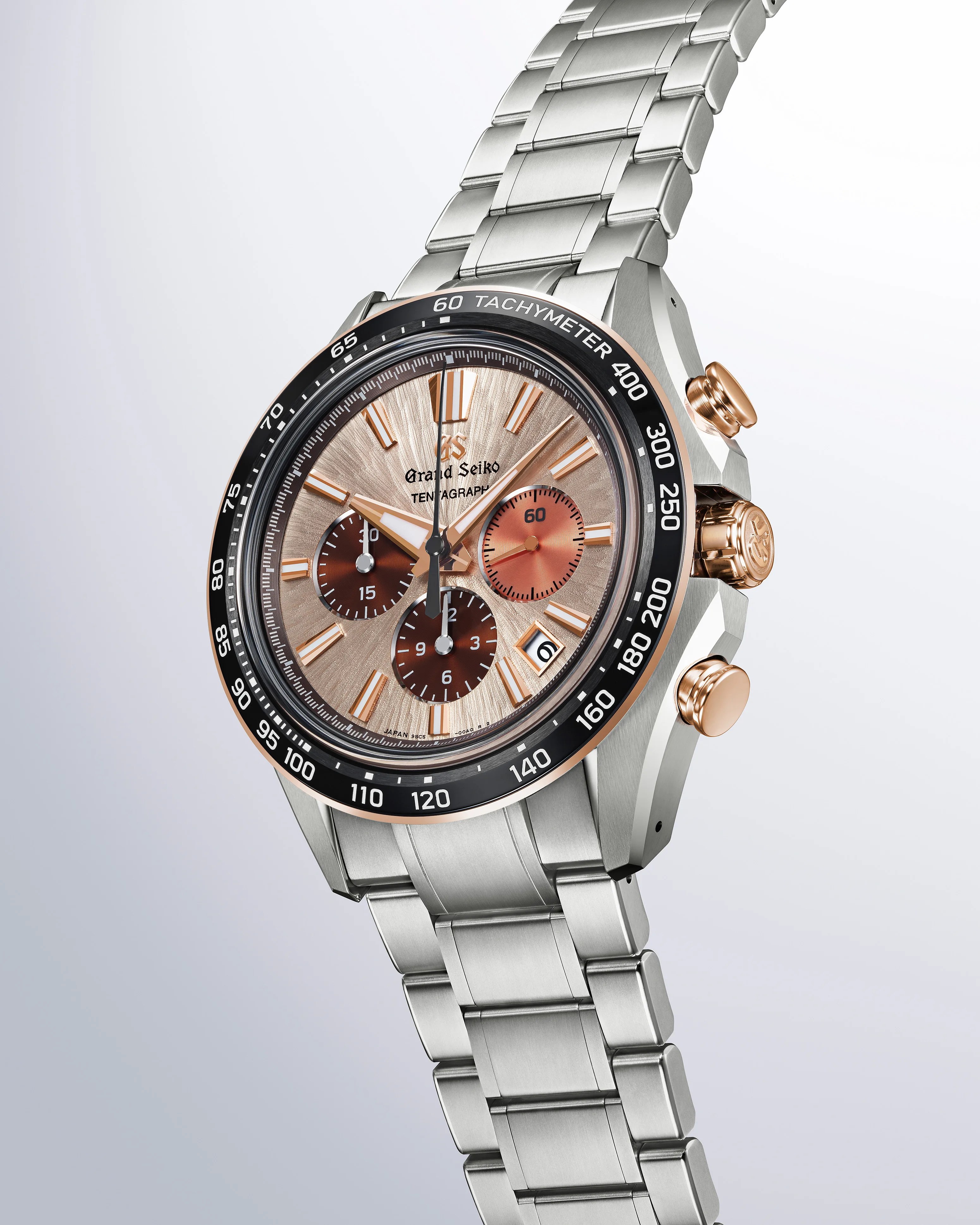 Grand Seiko chronograph watch with a silver stainless steel bracelet and case. The watch face features a textured beige dial with rose gold hour markers and hands, three subdials in shades of brown and copper, a date window at 4 o'clock, and a black tachymeter bezel with white markings. The crown and pushers are rose gold.