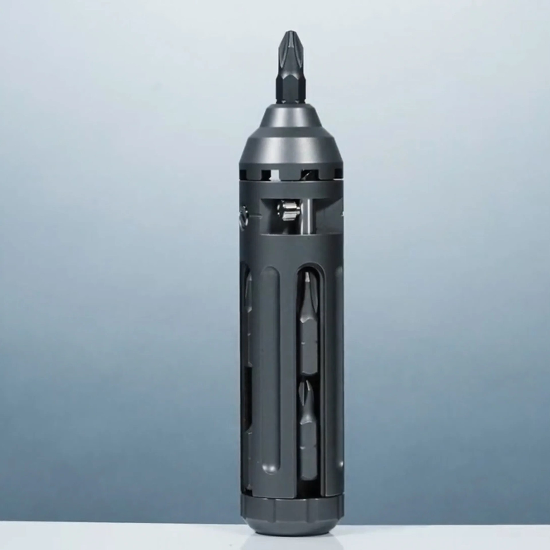 Compact black multi-bit screwdriver with a cylindrical body featuring slots that hold various screwdriver bits, and a bit attached at the top.