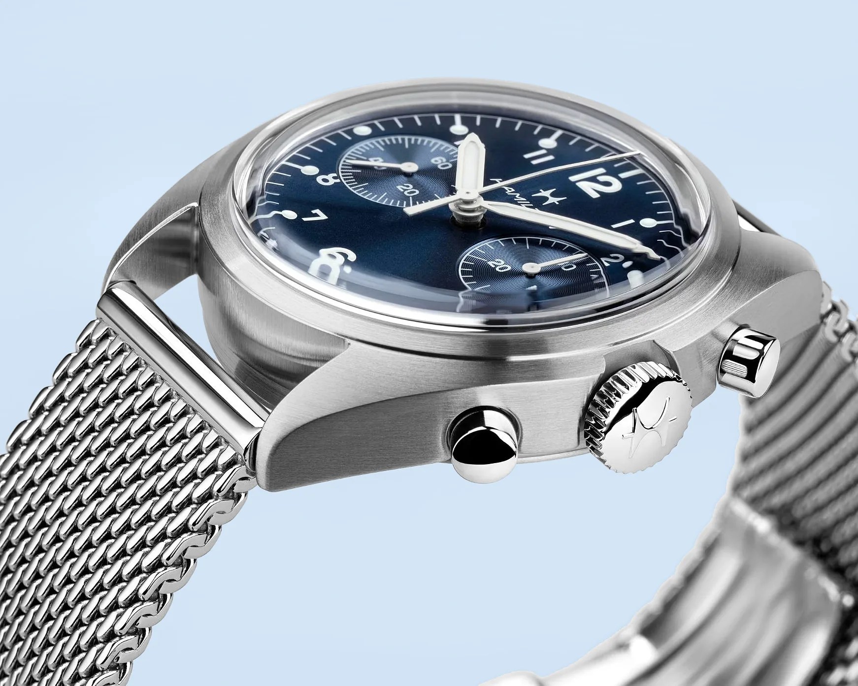 Stainless steel wristwatch with a blue dial featuring two subdials, white hour markers, and hands. The watch has a polished crown with an engraved star logo and two push buttons on the side. It is paired with a silver mesh metal strap. The watch face is covered by a domed crystal.