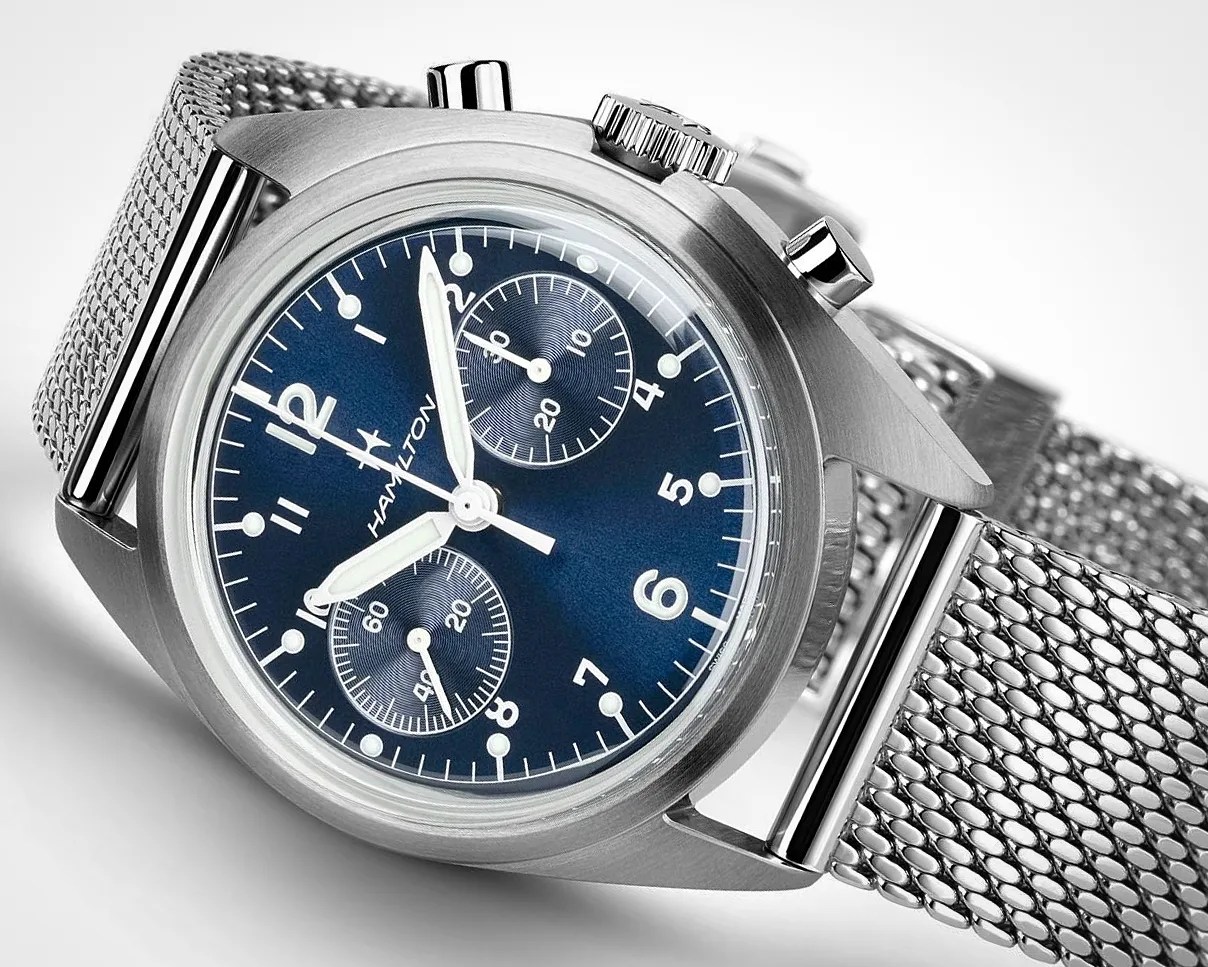 Steel wristwatch with a blue dial featuring white numerals and markers, two subdials, and luminous hands. The watch has a stainless steel mesh band and a brushed metal case with two push buttons and a crown on the right side. The brand name "Hamilton" is visible on the dial.