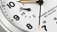 Close-up of a white watch face showing black numerals 7, 8, 9, and 10, with beige and black hour and minute hands. There is a smaller gauge with a black hand indicating fuel or power reserve, marked with "F," "1/2," and "E" in red and black. Text on the watch face reads "POWER RESERVE 80 HOURS." The second hand is thin and black with a beige tip.