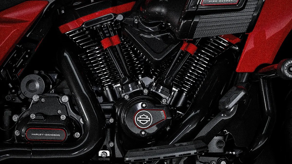 Close-up of a Harley-Davidson motorcycle engine, featuring black and red components with visible branding on the engine cover and surrounding parts. The engine has a V-twin configuration with prominent cooling fins and a sleek, polished finish.