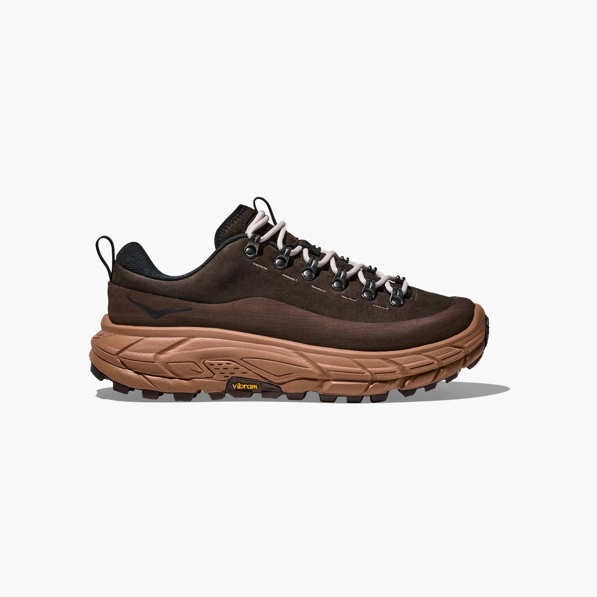 Dark brown hiking shoe with a thick, textured light brown sole featuring Vibram branding. The shoe has black and white laces threaded through black metal eyelets, a black padded collar, and a black pull tab at the heel. The upper material appears to be suede or nubuck with a subtle wave design and a small black logo on the side.