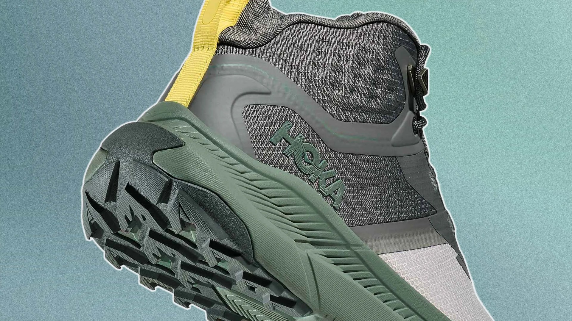 Gray and green Hoka hiking shoe with a yellow pull tab, featuring a rugged sole and mesh upper.