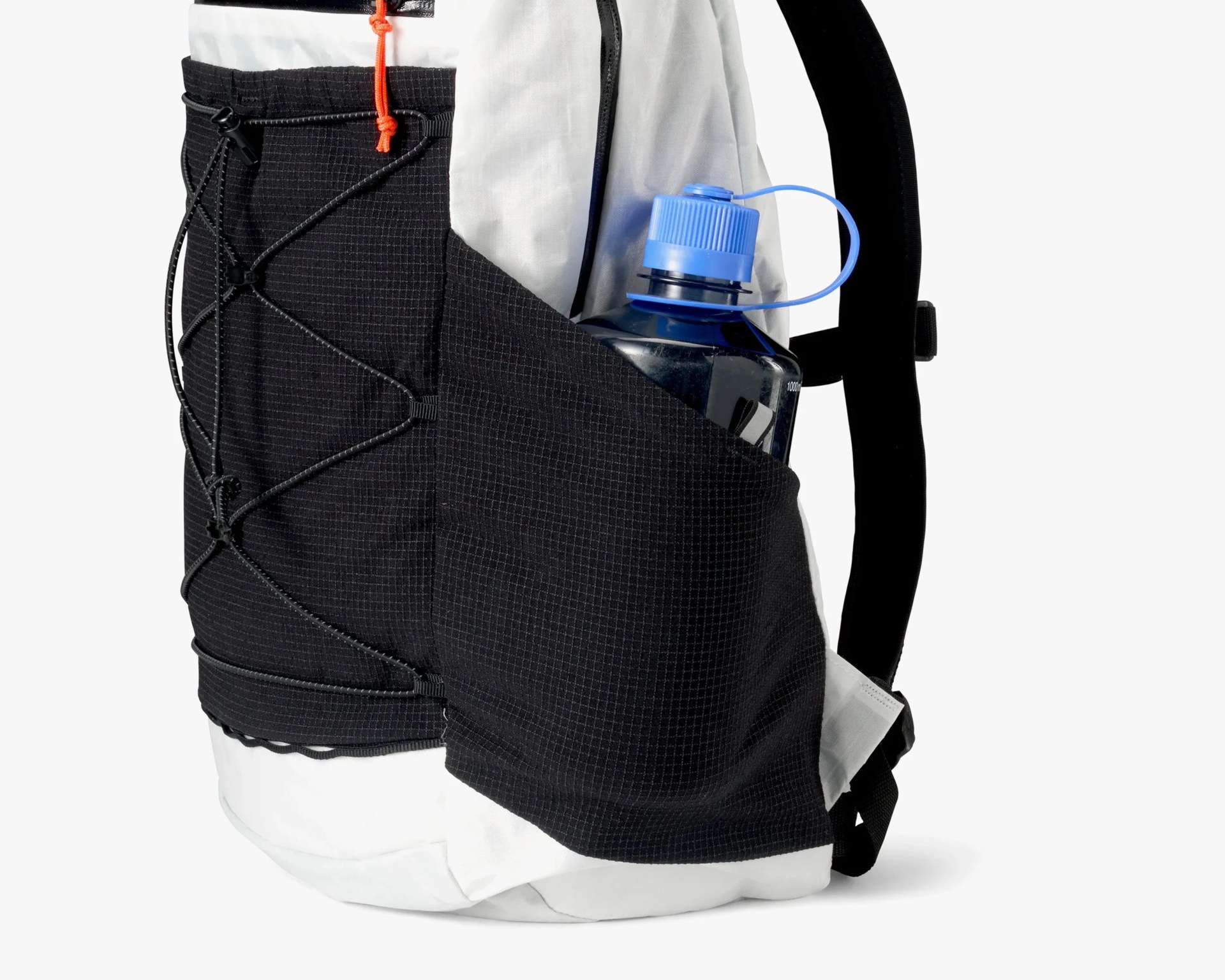 Side view of a white and black backpack featuring a large black mesh side pocket holding a blue water bottle with a screw-on cap. The black section of the backpack has a crisscrossed elastic cord for additional storage or securing items. The backpack has a padded black shoulder strap visible on the right side.