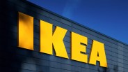 Large yellow letters spelling "IKEA" mounted on a dark blue tiled exterior wall under a clear blue sky.