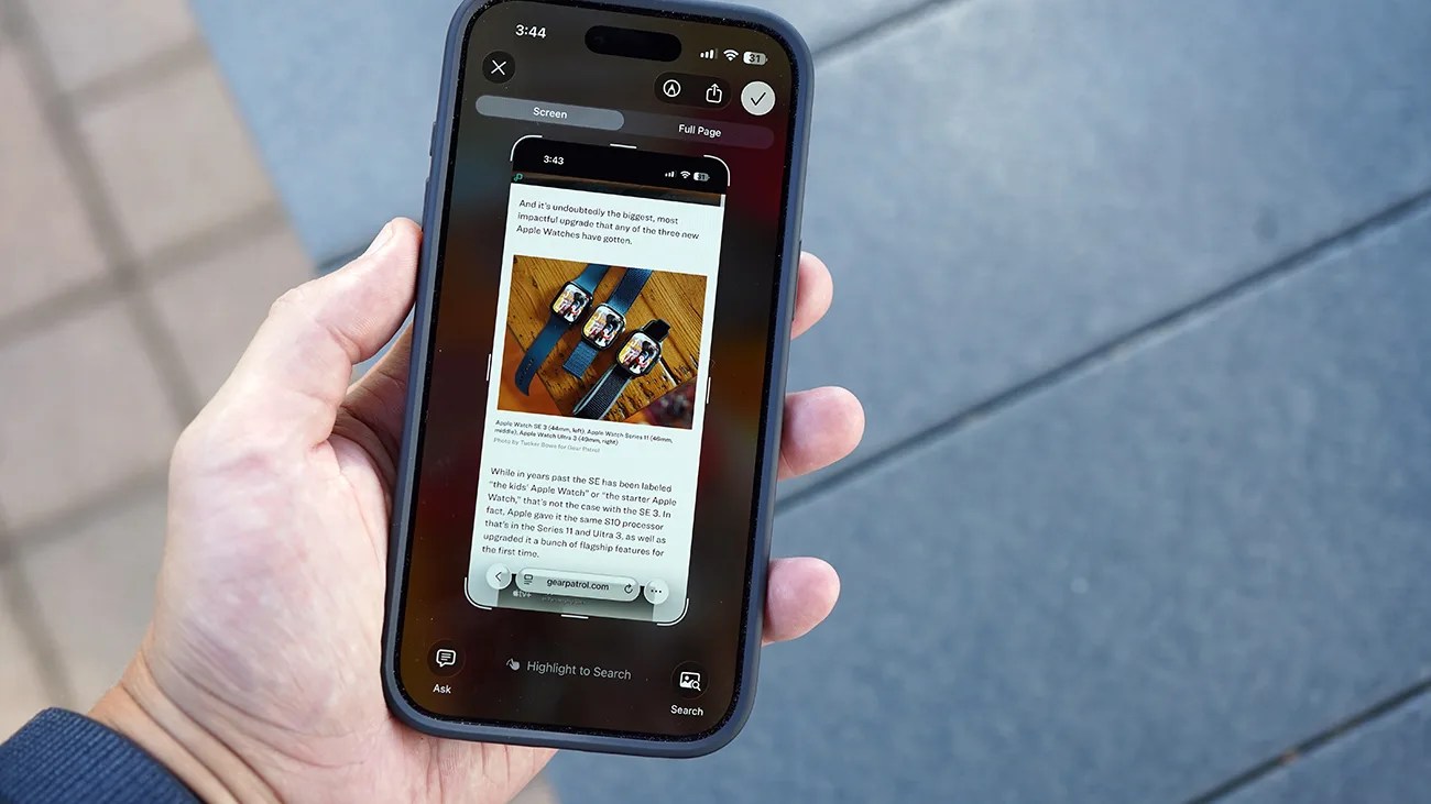 A hand holding a smartphone displaying a screenshot of a webpage about Apple Watches, showing images of three Apple Watches with different bands on a wooden surface. The phone screen shows options for capturing the screen or full page, with buttons for "Ask," "Highlight to Search," and "Search" visible at the bottom. The background is a tiled floor with blue and gray tones.