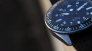 Close-up of a black tool watch with a rotating bezel marked in white numerals and indices. The watch face features large white hour markers, bold hands with a prominent arrow-shaped hour hand, and an orange-tipped second hand. The text "PRO AUTOMATIC 200m" is visible on the dial. The watch case is metallic with a polished finish, and it is attached to a black strap.
