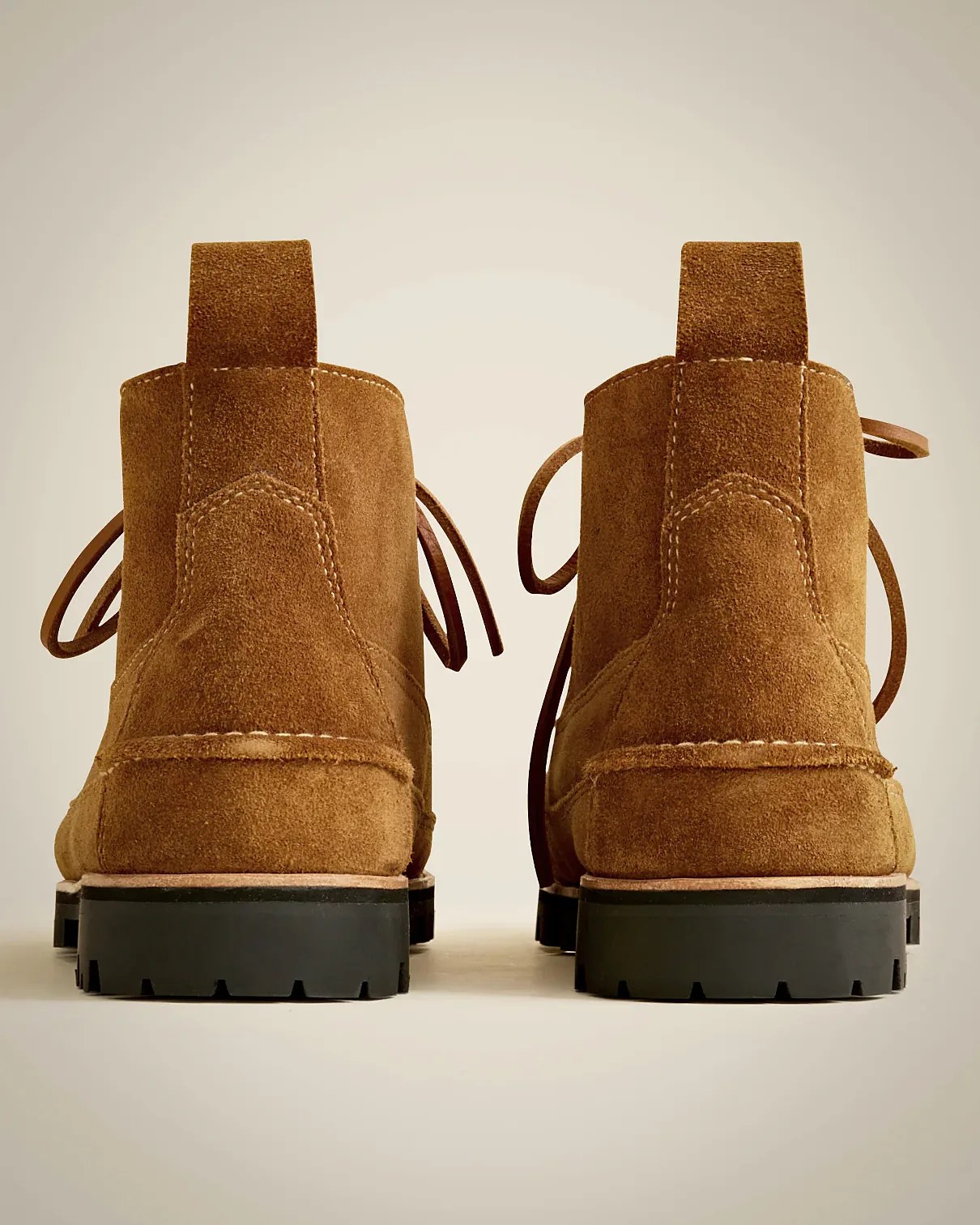 Pair of brown suede ankle boots with pull tabs at the back, visible stitching, and black rubber lug soles, shown from the rear.