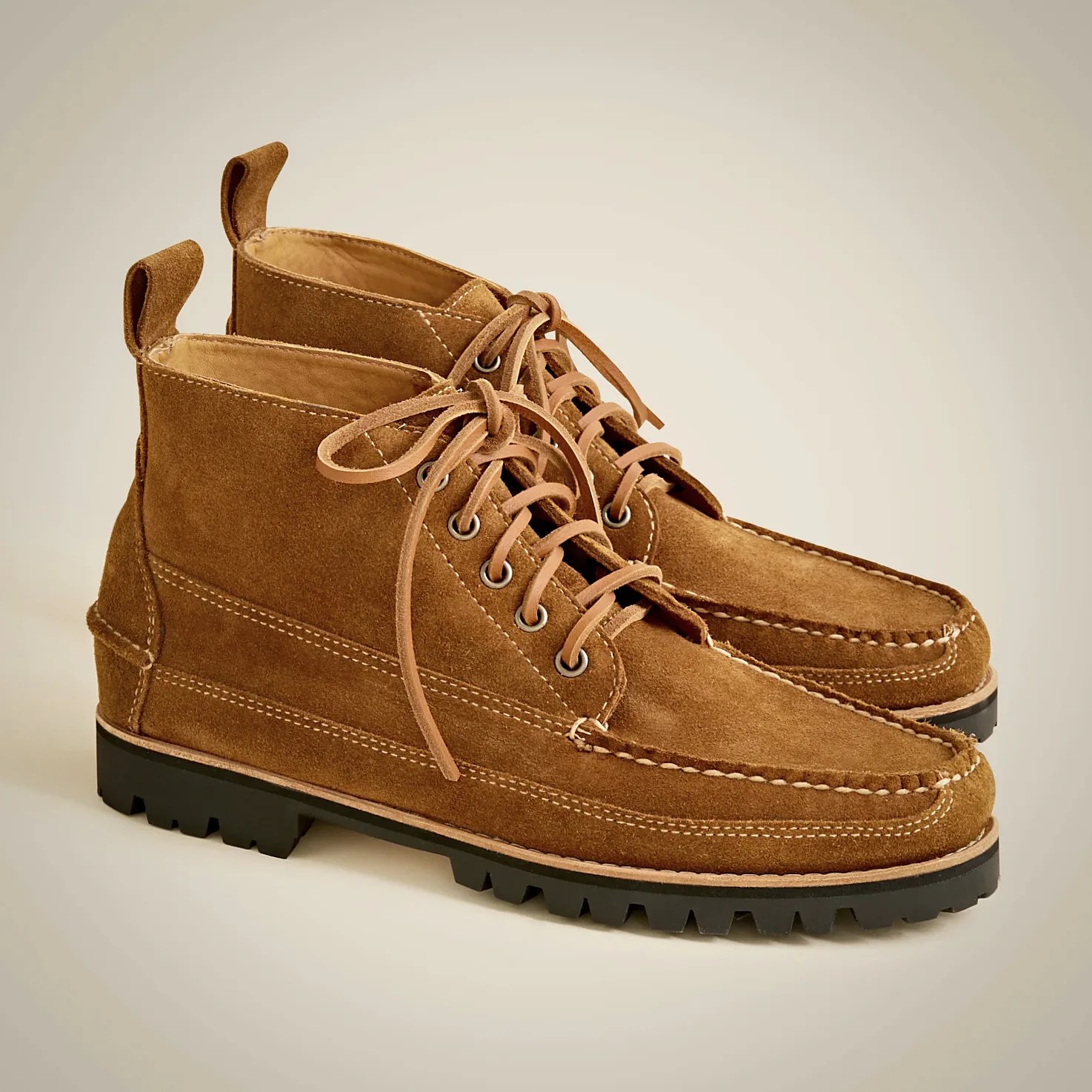 Pair of brown suede lace-up boots with moc toe stitching, metal eyelets, pull tabs at the back, and black lug soles.