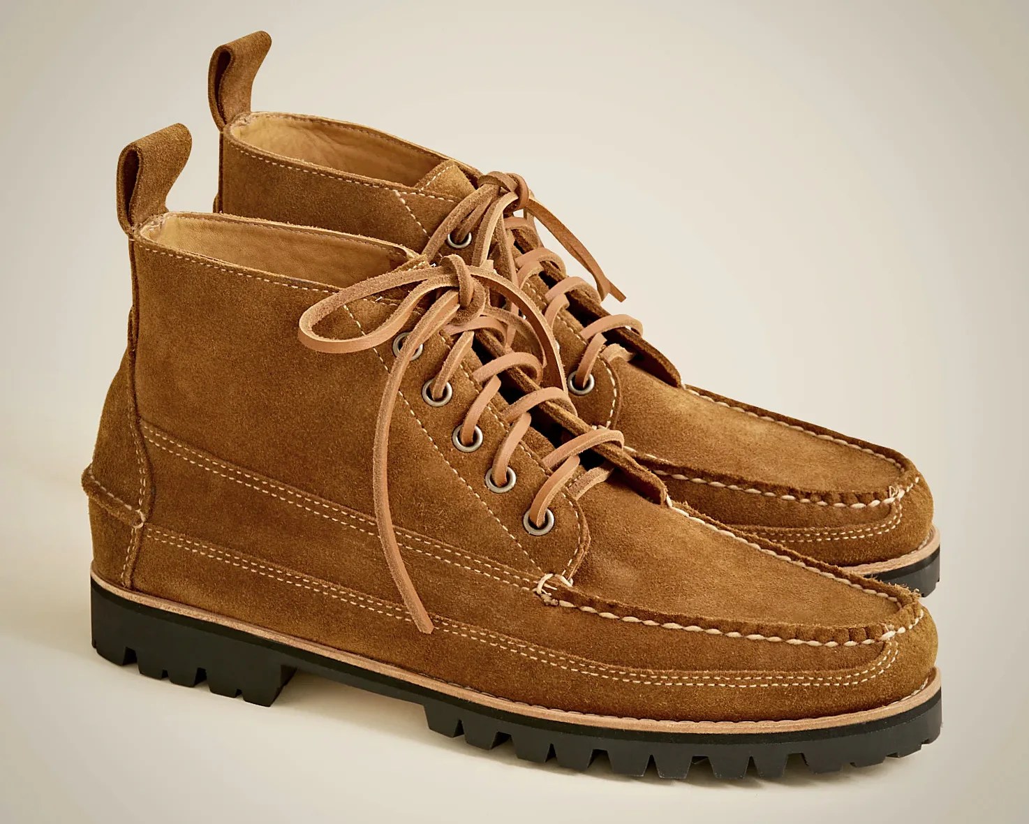 Brown suede lace-up boots with moc toe stitching, metal eyelets, and black lug soles. The boots have pull tabs at the back and visible white stitching details.