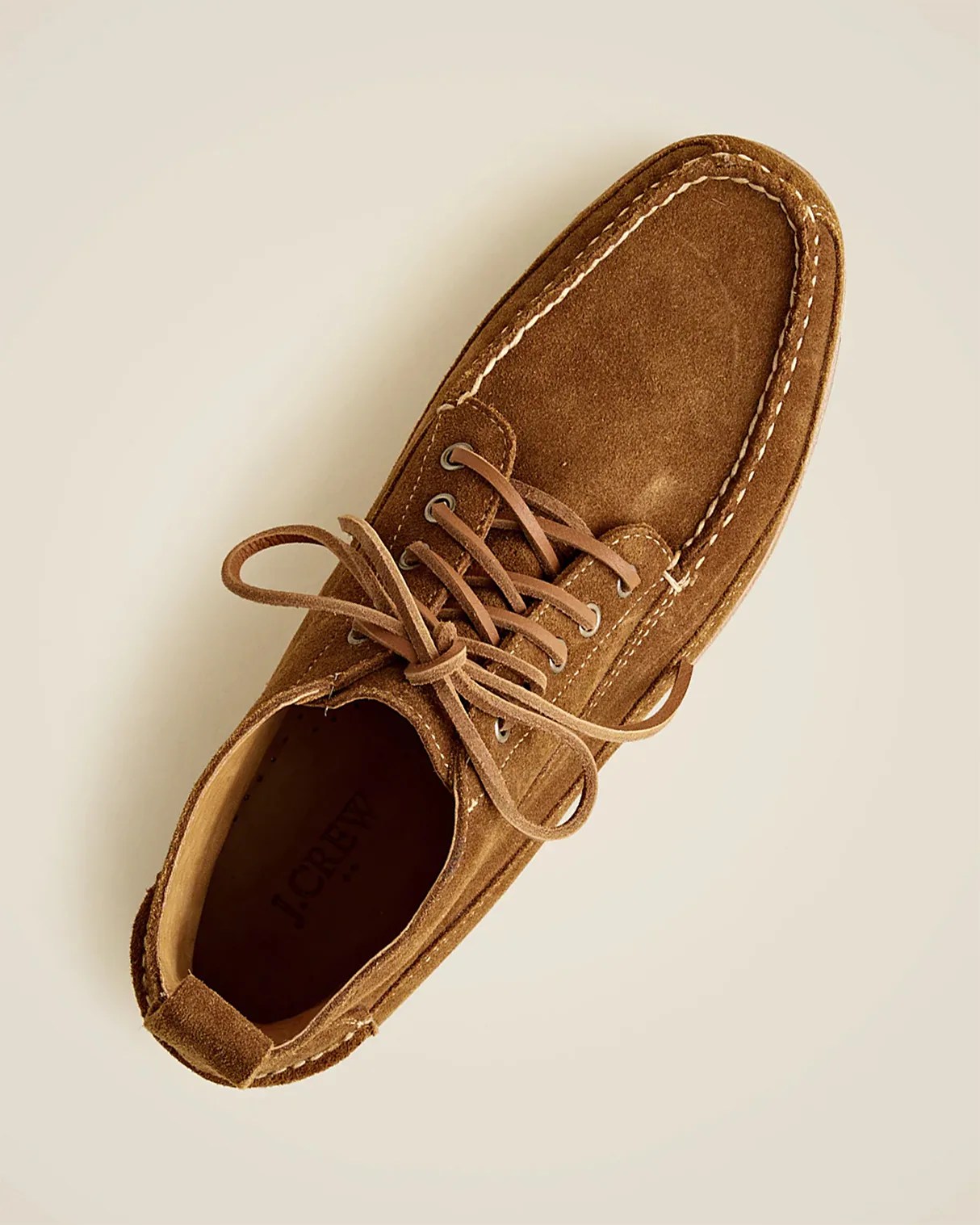 Brown suede lace-up shoe with white stitching details and a rounded toe, viewed from above. The interior is tan with the brand name "J.CREW" visible inside. The shoe has a casual, moccasin-inspired design.