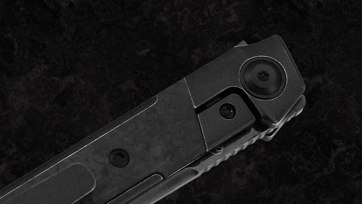 Close-up of a black folding knife's hinge and locking mechanism, showing the textured handle and screws against a dark, marbled background.