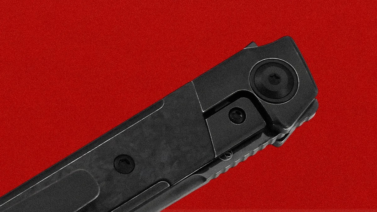 Close-up of the top part of a black folding knife with a textured handle and visible screws, set against a solid red background.