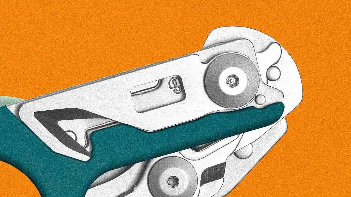 Close-up of a metal and teal-colored mechanical tool against an orange background, showing intricate components including screws, a lever, and a small window with the number "9" visible.