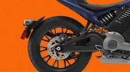 Rear section of a motorcycle featuring a black alloy wheel with a disc brake and Brembo caliper, a black swingarm, a visible rear suspension spring, and part of the engine casing, set against an orange background.