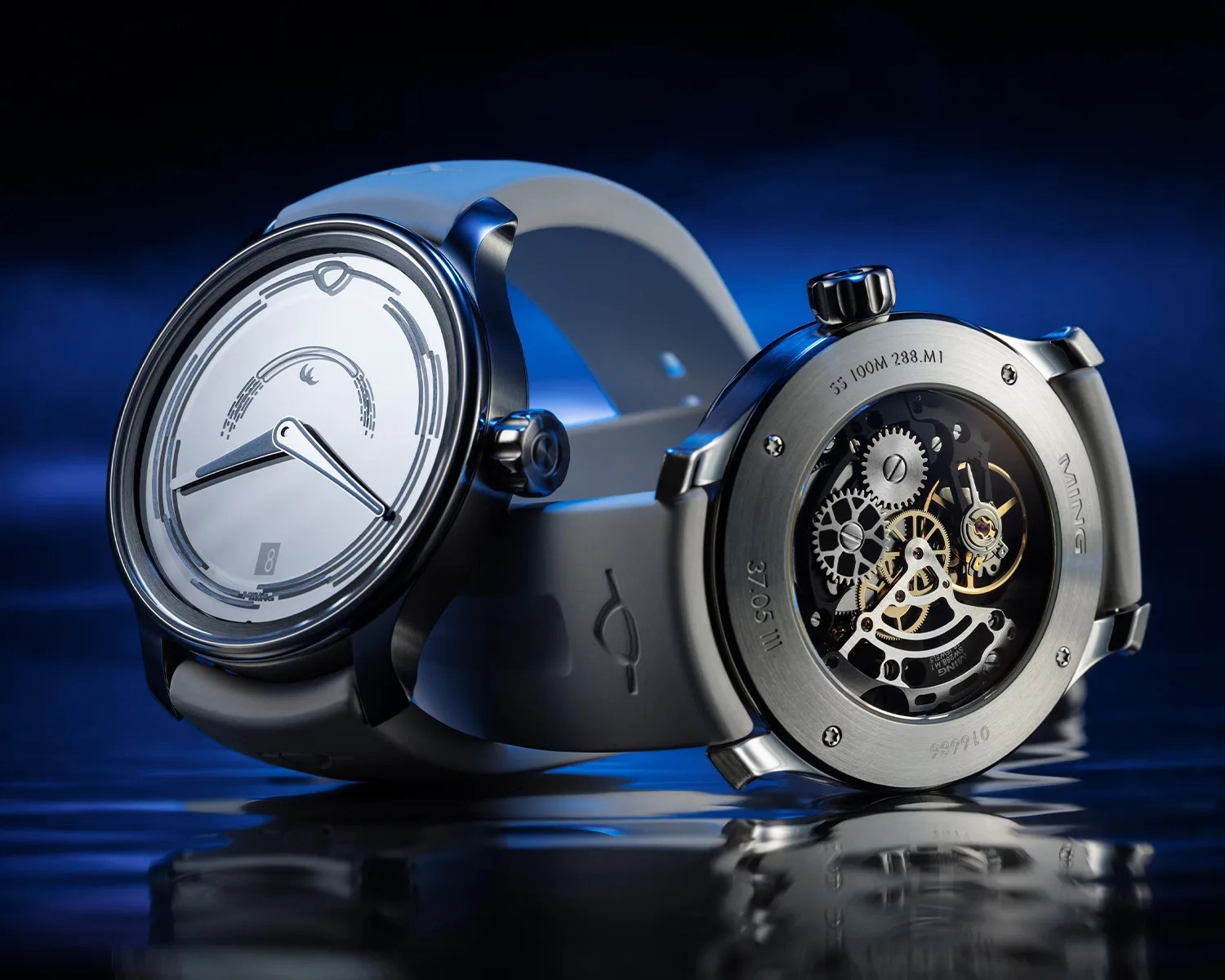 Two modern wristwatches with white straps are displayed against a blue background. One watch shows a minimalist dial with hour and minute hands and a small date window at the 6 o'clock position. The other watch is positioned to reveal its transparent case back, showcasing intricate mechanical gears and components. The brand name "MING" is engraved on the back.