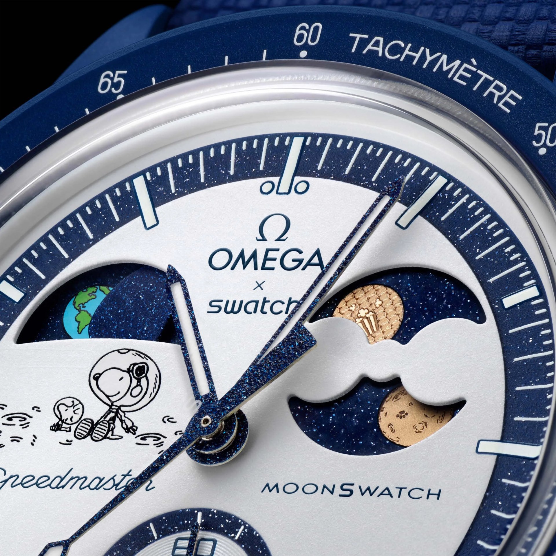 Close-up of an Omega x Swatch Speedmaster MoonSwatch watch face featuring a blue and white color scheme. The dial includes a small illustration of Snoopy in an astronaut suit, Earth and moon motifs, and blue speckled hands. The tachymeter scale is visible on the blue bezel.