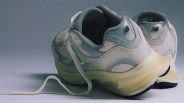 Pair of light gray and white New Balance sneakers with mesh and suede detailing, featuring white laces and a slightly yellowed sole, positioned with the heels facing forward.