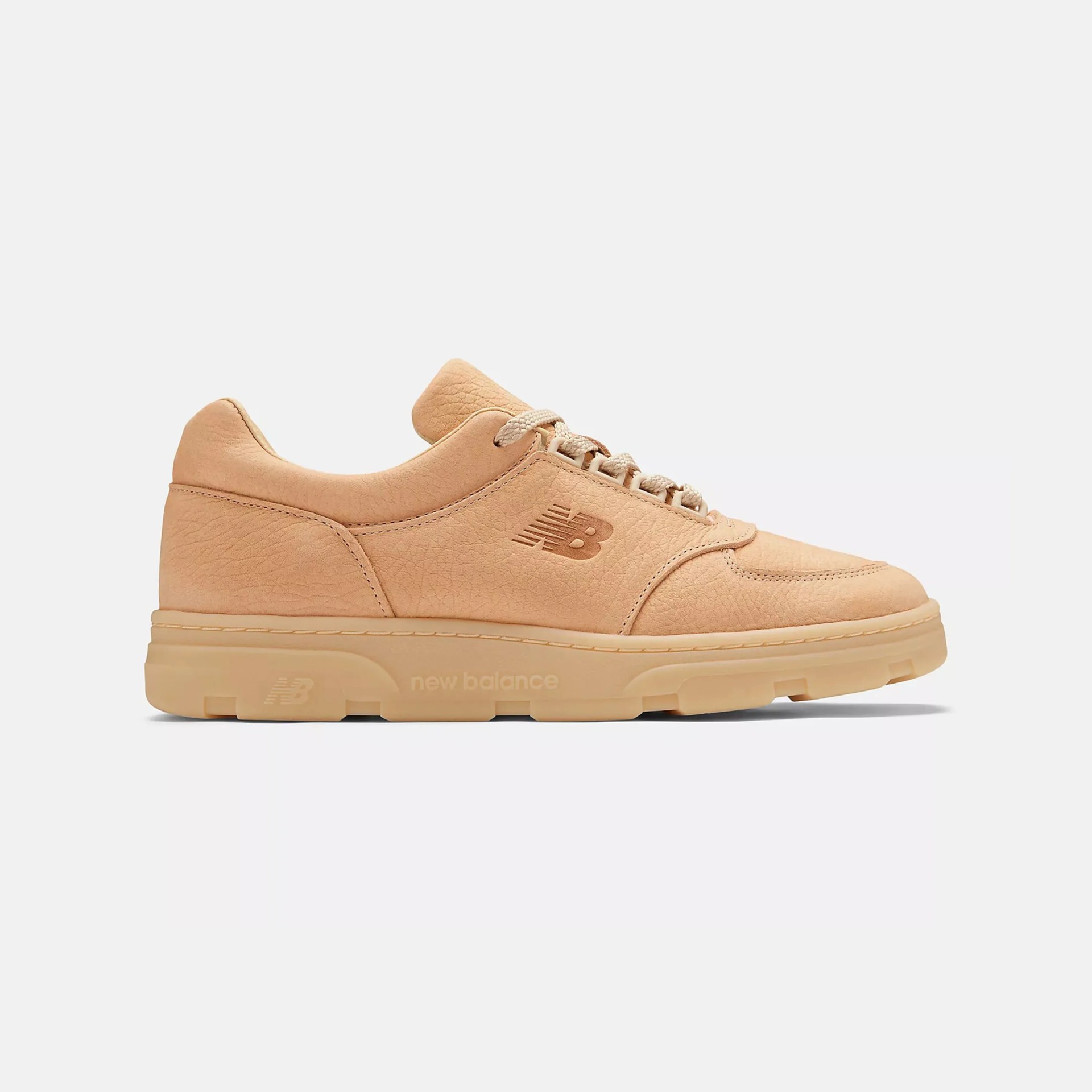 Light tan New Balance sneaker with a textured leather upper, matching laces, and a thick rubber sole. The New Balance "NB" logo is embossed on the side, and "new balance" is embossed on the midsole. The shoe has a low-top design with visible stitching details.