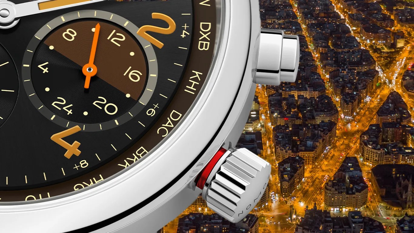 Close-up of a luxury watch face showing a 24-hour subdial with orange hands and gold numerals, encased in polished silver metal. The watch bezel features city abbreviations like DXB, KHI, DAC, and BKK, indicating world time zones. The crown and a push button are visible on the right side of the watch case. The background shows a nighttime aerial view of a city with illuminated streets and buildings.