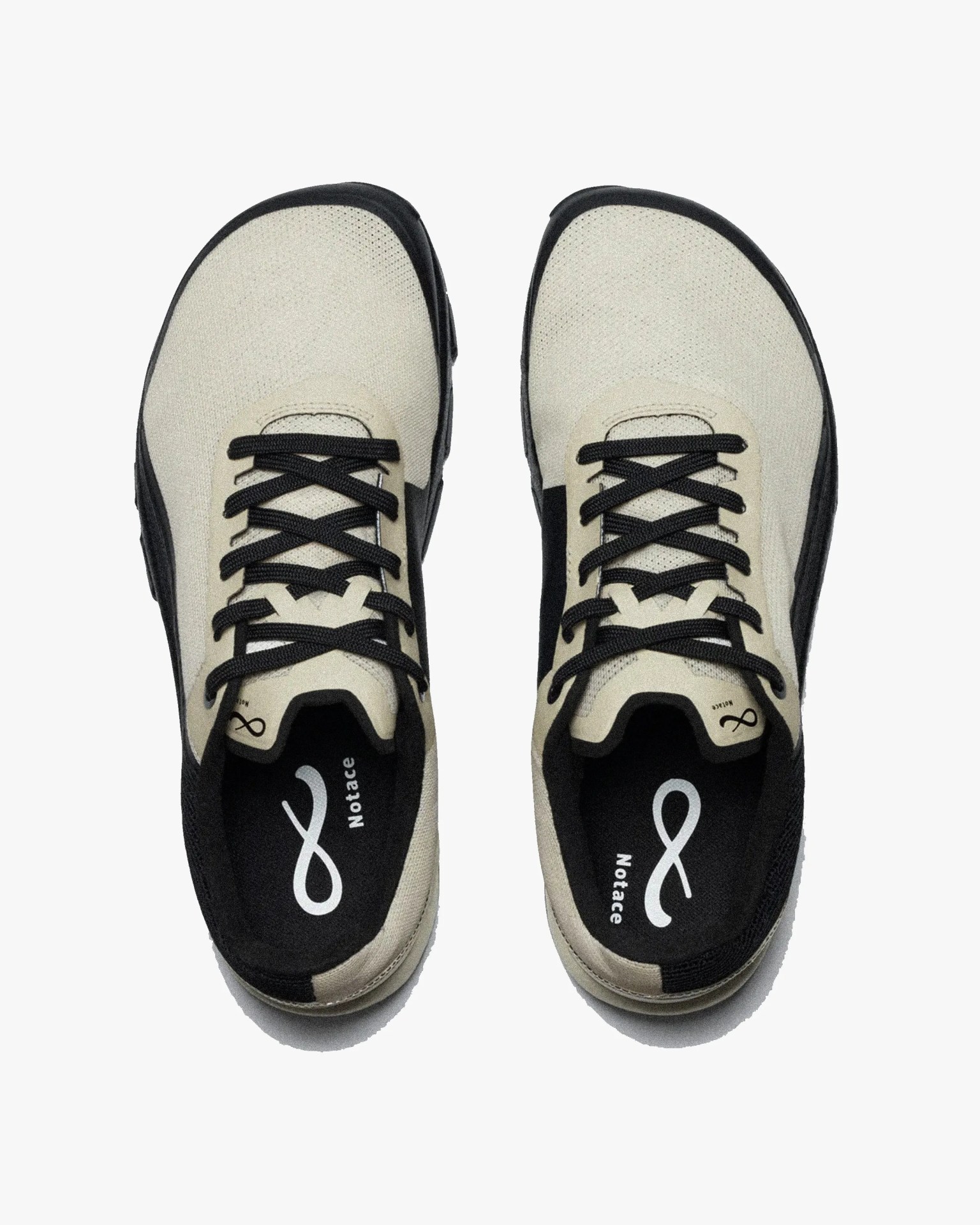 Pair of beige and black sneakers viewed from above, featuring black laces and black inner soles with a white infinity symbol and the word "Notace" printed on them. The sneakers have a mesh-like texture on the beige upper part and a black sole.