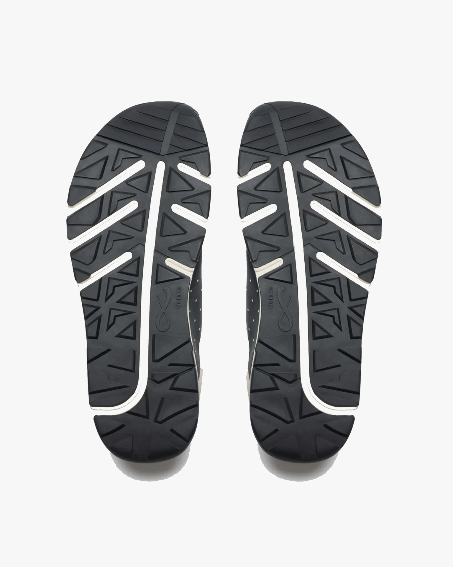 Black shoe soles with geometric tread patterns and white accents, shown from the bottom. The soles have a combination of triangular and linear grooves for traction. The brand name "Kotacc" is embossed near the center of each sole.