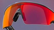 Sport sunglasses with a large, wraparound red-orange mirrored lens and a built-in camera on the left side near the nose bridge. The frame is black with a sleek, modern design. The lens has the word "PRIZM" printed on the lower right corner.
