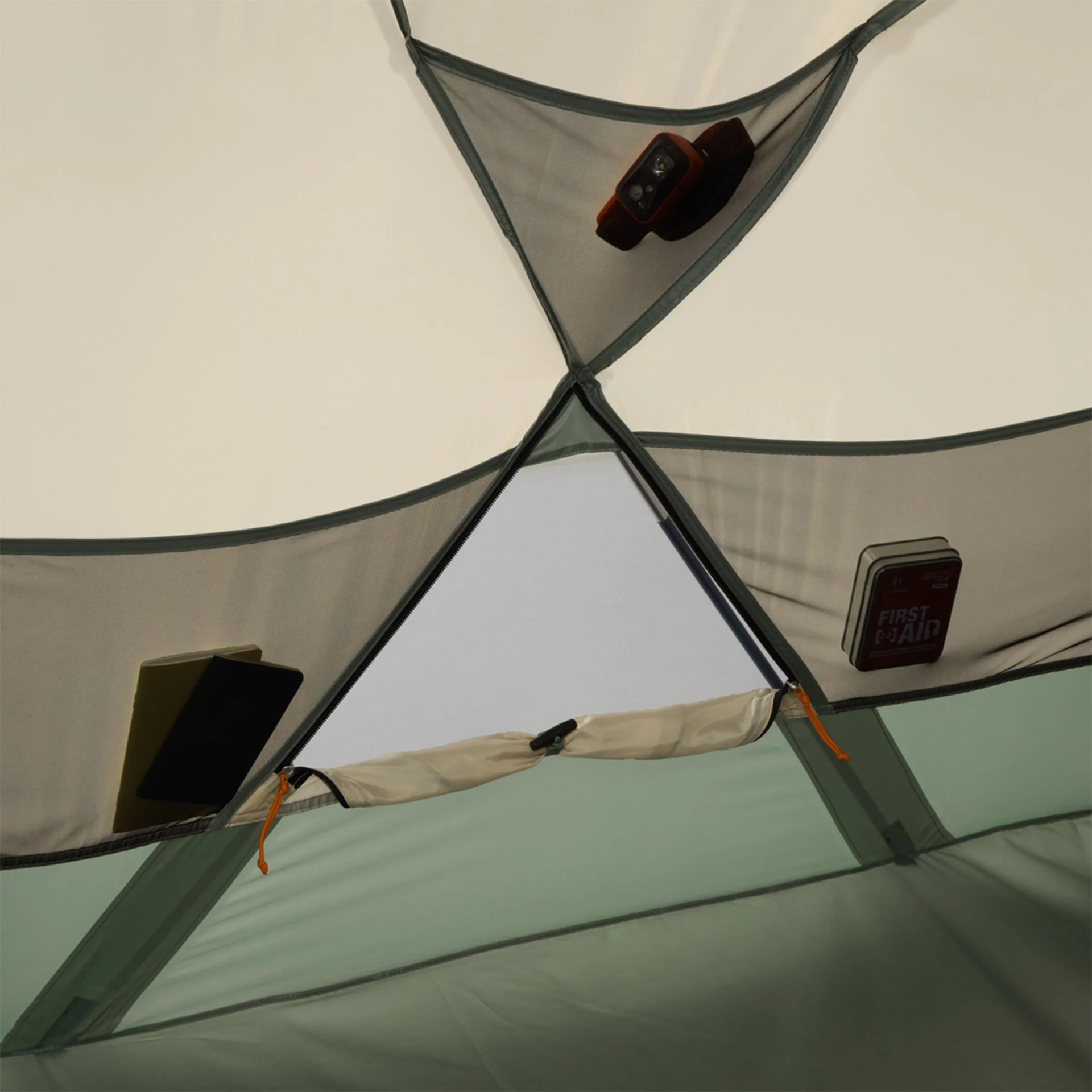 Mesh storage pockets attached to the ceiling of a tent, holding a flashlight, a book, and a first aid kit. The tent fabric is light beige and green.