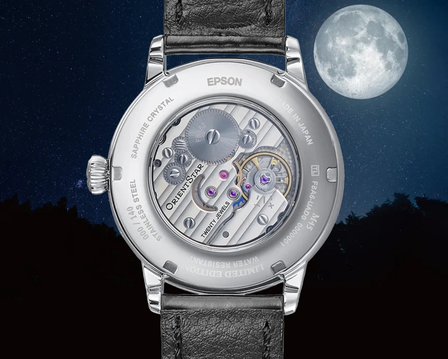 Back view of an Orient Star mechanical wristwatch with a stainless steel case and black leather strap, showcasing the intricate movement with visible gears and jewels through a sapphire crystal case back, set against a night sky background with a full moon. The case back is engraved with details including "EPSON," "SAPPHIRE CRYSTAL," "STAINLESS STEEL," "LIMITED EDITION," "WATER RESISTANT," and "MADE IN JAPAN.