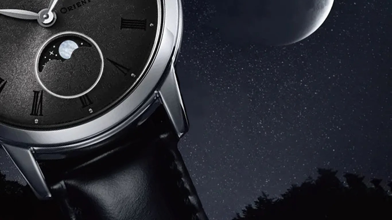Close-up of a wristwatch with a black textured dial, silver case, and black leather strap. The watch features Roman numeral hour markers and a moon phase indicator. The background shows a starry night sky with a partially visible moon and silhouetted treetops.