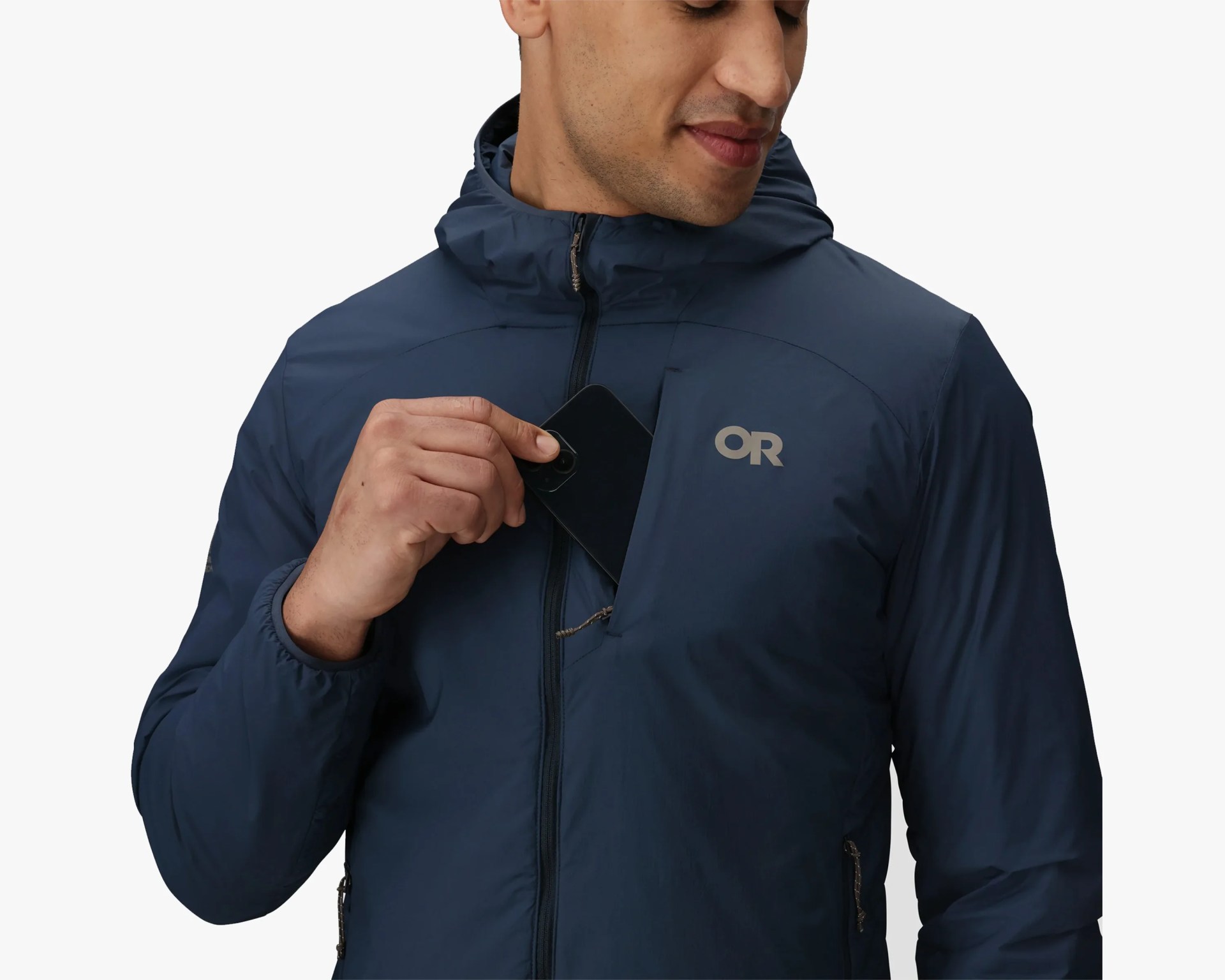 Man wearing a navy blue hooded jacket with a front zipper, placing a black smartphone into a zippered chest pocket on the left side, which features a reflective "OR" logo.