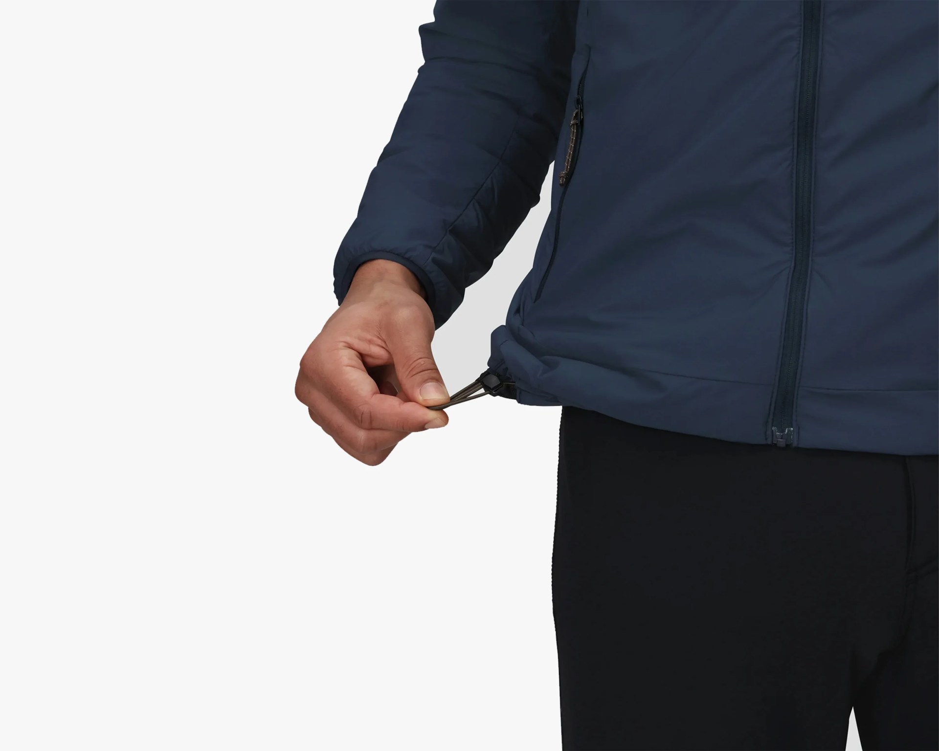 A person wearing a navy blue jacket is adjusting the drawstring at the bottom hem of the jacket with their left hand. The jacket has a visible zipper and a zippered pocket on the side. The person is also wearing black pants.