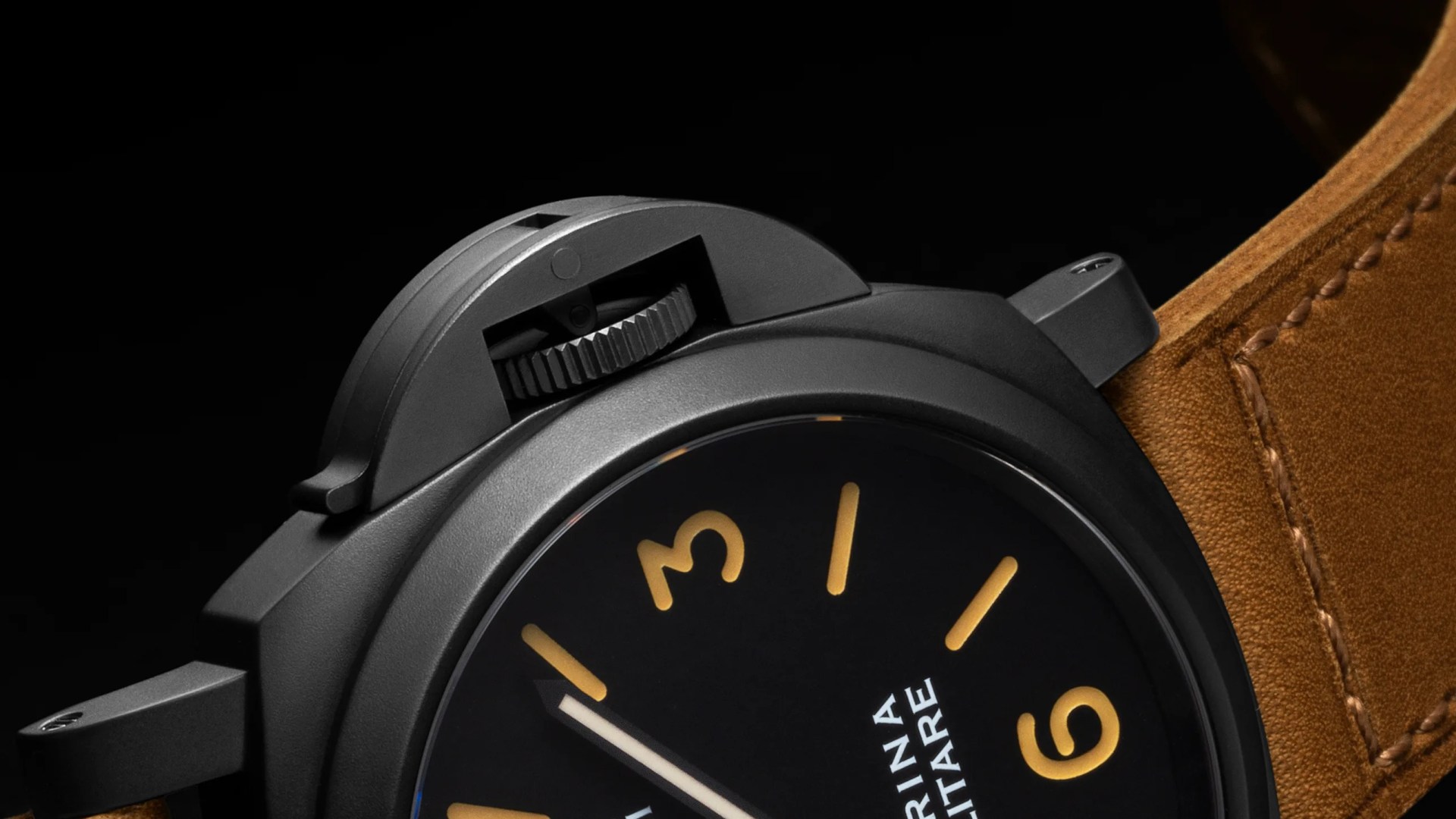 Close-up of a black wristwatch with a matte finish case, featuring a black dial with large, yellowish-orange numerals and markers. The watch has a distinctive crown guard and a brown leather strap with visible stitching. The dial shows partial text "MARINA MILITARE.