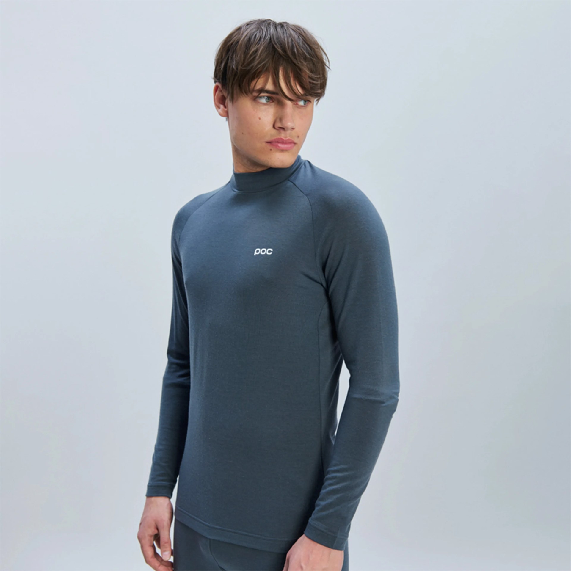 Slim-fit, long-sleeve, high-neck athletic top in dark gray with a small white "poc" logo on the left chest, worn by a young man with short brown hair looking to his left.