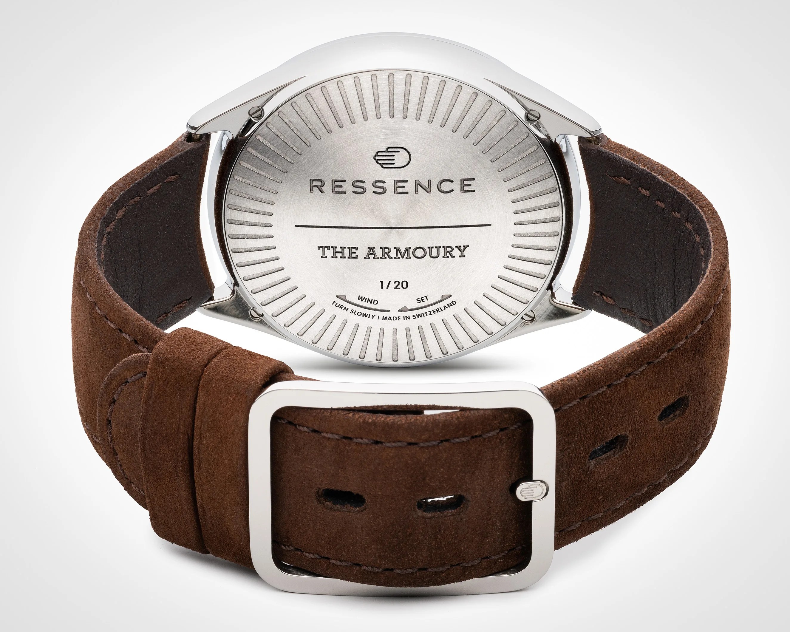 Back view of a Ressence wristwatch with a polished silver case and engraved markings. The case back features the brand name "RESSENCE," the model name "THE ARMOURY," and the limited edition number "1/20." Instructions for winding and setting the watch are also engraved, along with "TURN SLOWLY | MADE IN SWITZERLAND." The watch has a brown suede leather strap with visible stitching and a polished silver buckle.