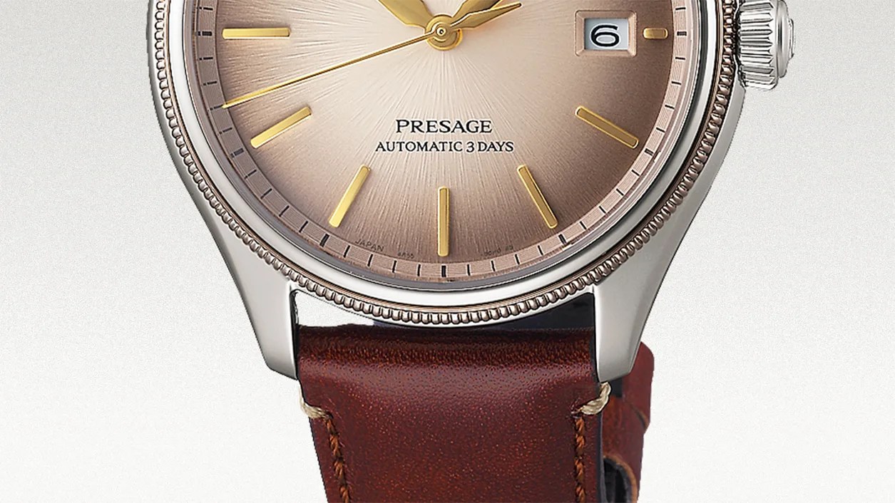 Close-up of a wristwatch with a brown gradient dial featuring gold hour markers and hands, a date window at 3 o'clock, and the text "PRESAGE AUTOMATIC 3 DAYS." The watch has a polished silver bezel with a textured edge and a brown leather strap with visible stitching.