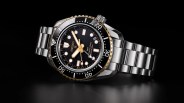 Seiko diver's watch with black dial, gold accents, and stainless steel bracelet on black background.
