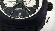 Close-up of a black chronograph watch face with green and white hands and markers. The dial features two subdials with white backgrounds and black markings. Text on the dial reads "CERAMOD+ CHRONOGRAPH 100M | 330FT" and "AUTOMATIC" above and below a date window displaying the number 25. The watch case has a matte black finish with a textured crown and a white pusher with a green ring on the side.