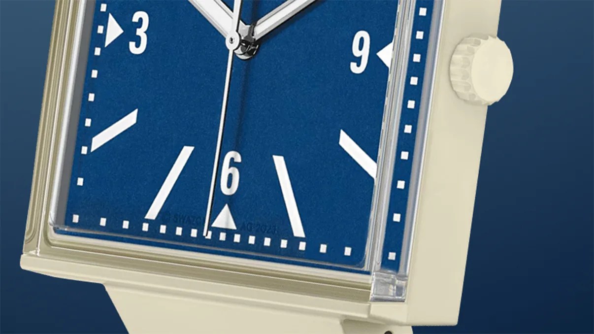 Square wristwatch with a blue face, white hour markers, and white hands. The watch case and strap are cream-colored, and there is a ridged crown on the right side. The time displayed is approximately 12:08:30.