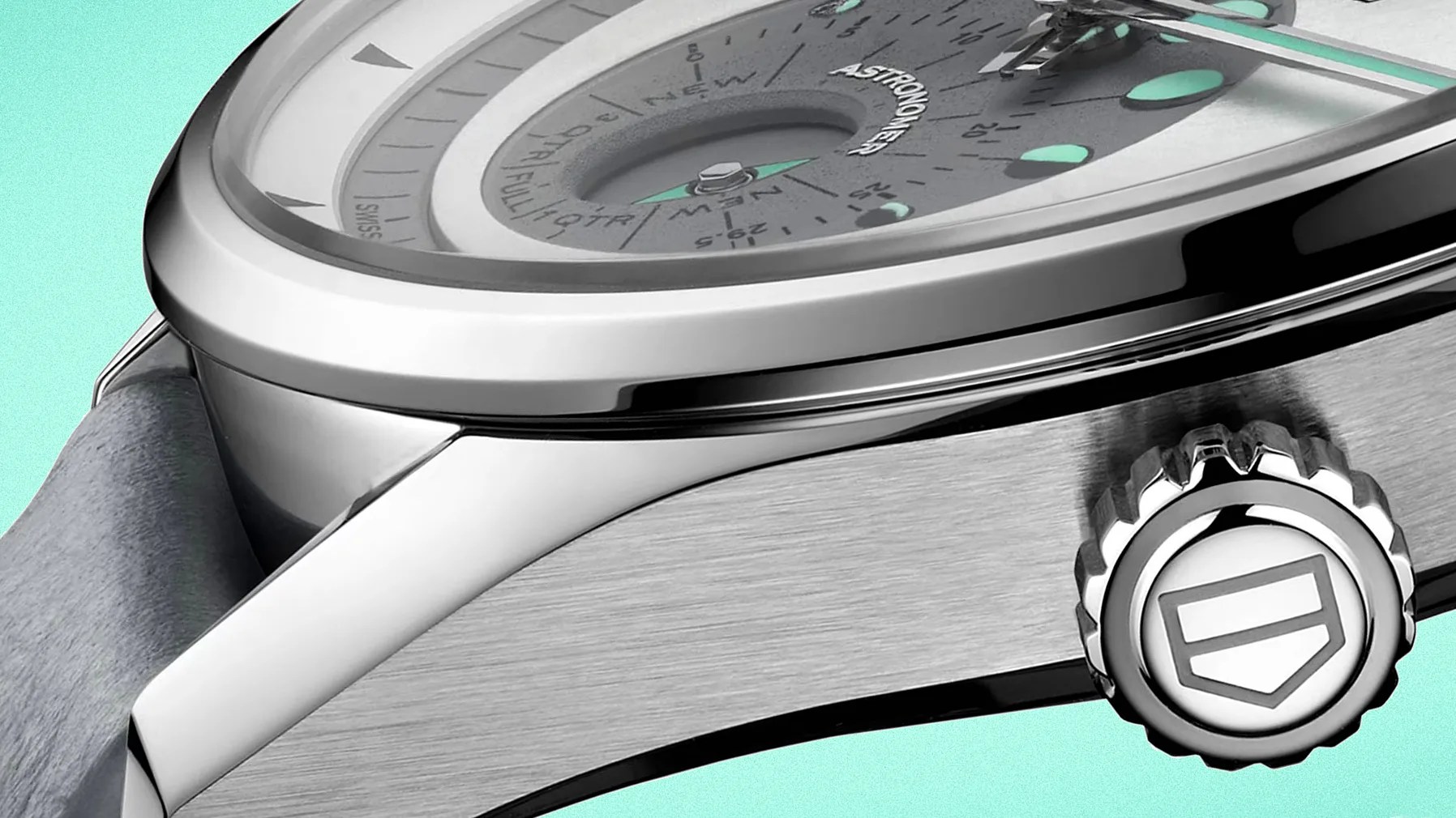 Close-up of a silver wristwatch case with a brushed metal finish and a polished bezel. The watch face features a detailed dial with the word "ASTRONOMER" visible, and the crown has a distinctive logo with a shield-like design. The watch strap appears to be made of leather.