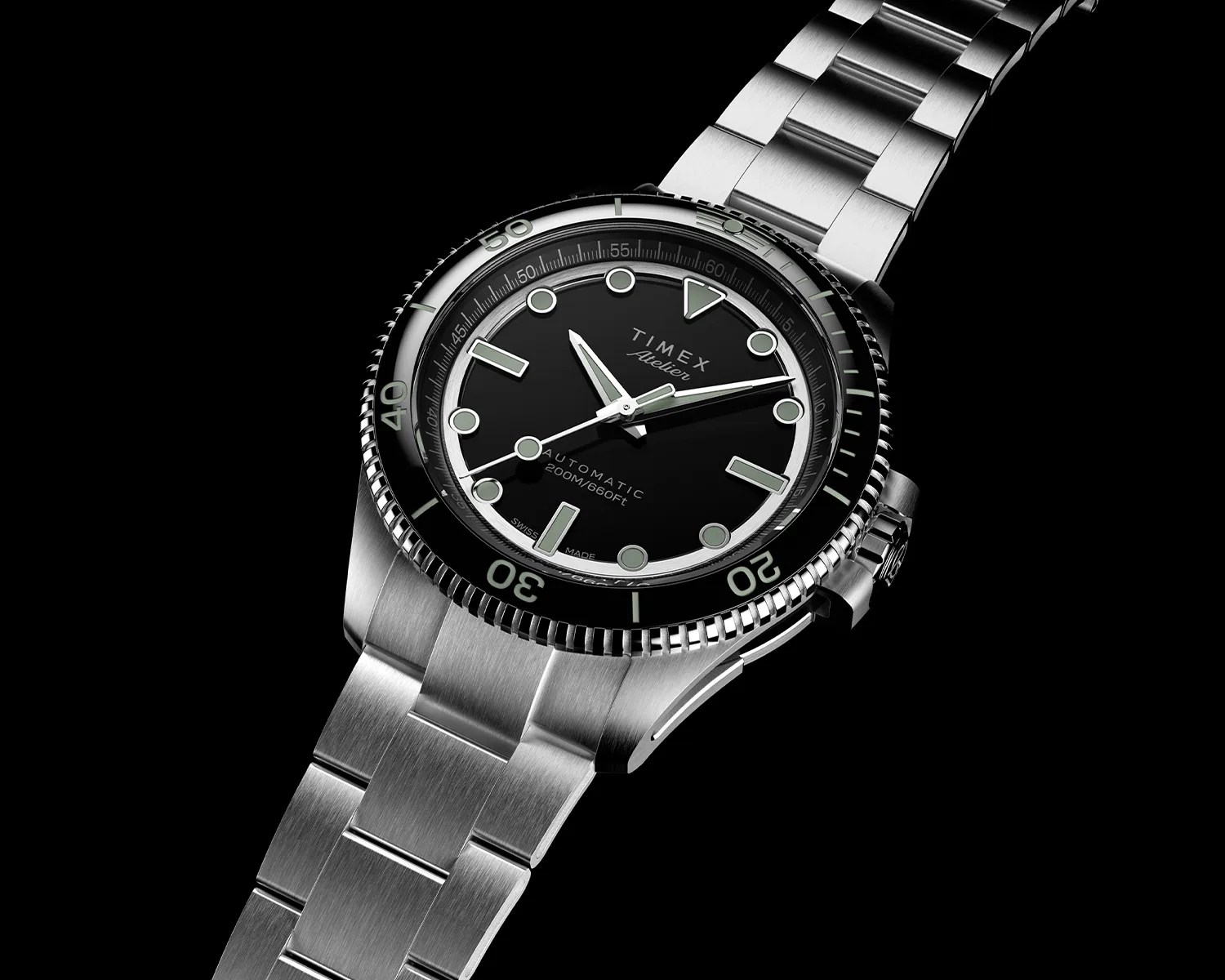 Stainless steel Timex wristwatch with a black dial and bezel, featuring luminous hour markers and hands. The watch has a brushed metal link bracelet and a rotating bezel with minute markings. The dial includes the text "TIMEX Atelier," "AUTOMATIC," and "200M/660FT," indicating water resistance. The watch crown is positioned on the right side.